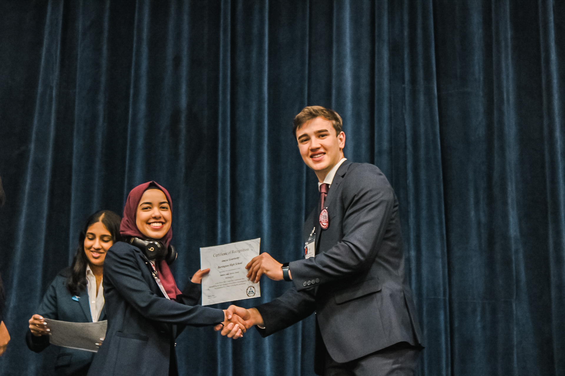 A member receives a Certificate of Recognition on stage at an Illinois HOSA event